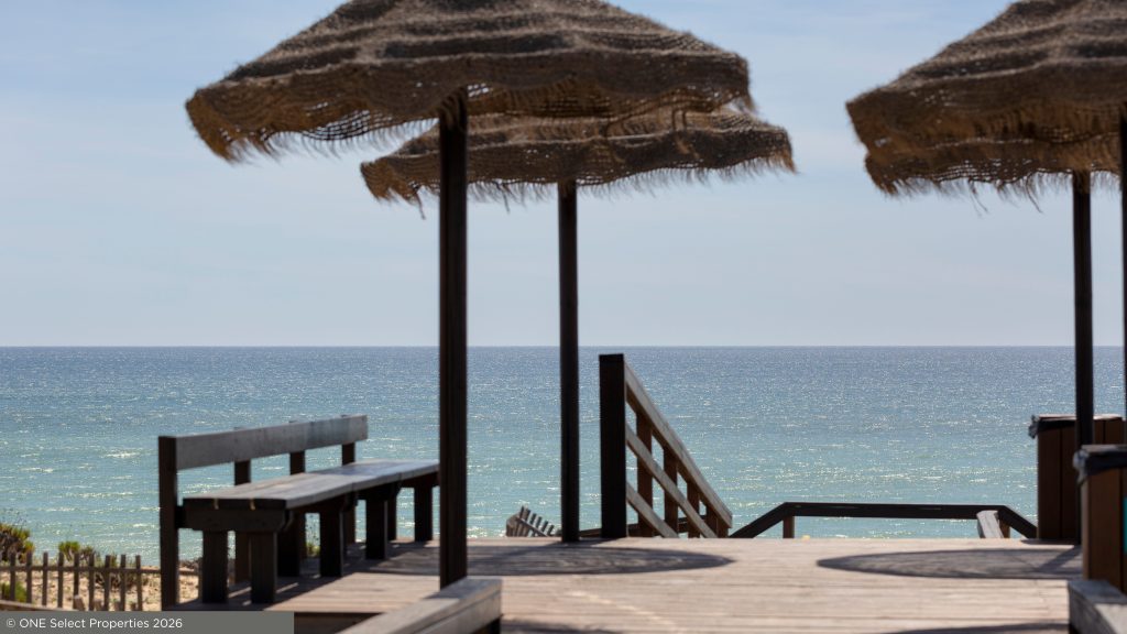 Wooden beach deck with straw parasols and steps leading down towards the sea in the Algarve.