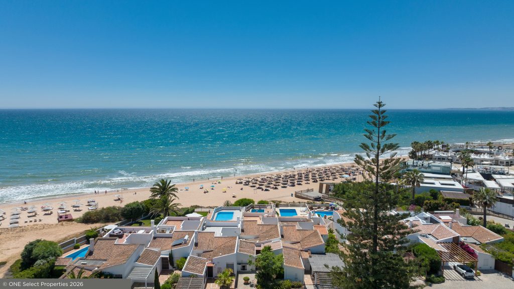 Elevated view of a beachfront residential area in the Algarve with turquoise sea, sandy beach and sun loungers.