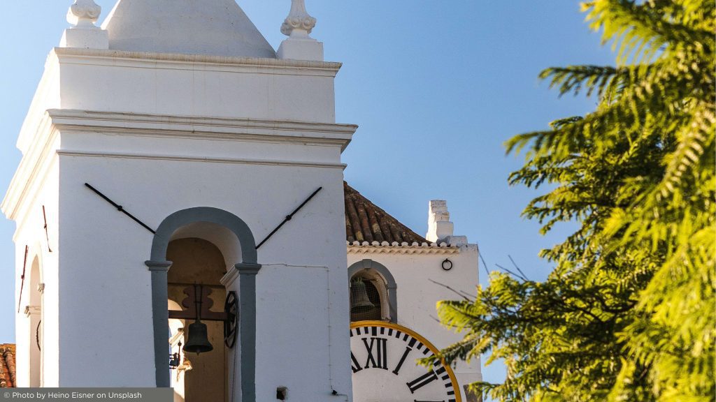 photo of a clock on a white building with a church top close by