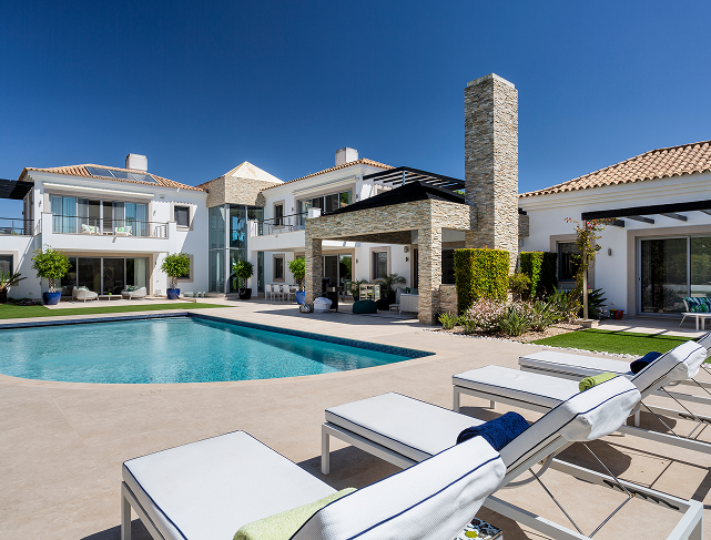 Contemporary luxury villa exterior with a blue swimming pool and white sun loungers.