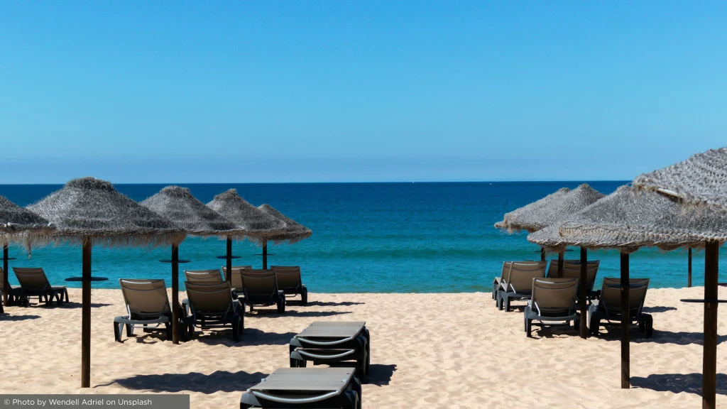 Espreguiçadeiras e chapéus de colmo numa praia algarvia com vista para o Atlântico